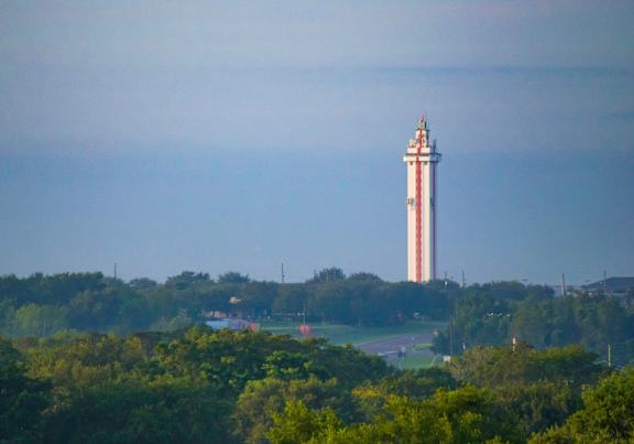 A lighthouse stands tall in the distance, surrounded by greenery.