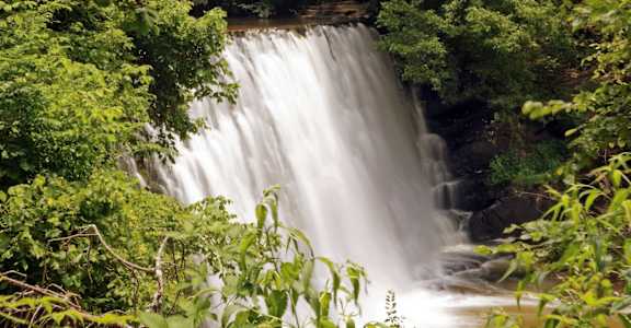 A waterfall cascades down a rocky cliff surrounded by lush green foliage.