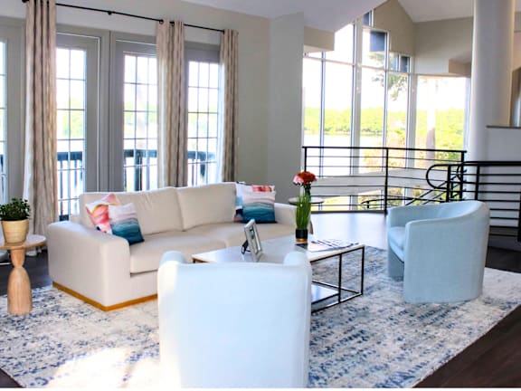 A white sofa with a red pillow is in the middle of a room with a large window.