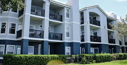 A large white and blue apartment building with balconies and a green lawn in front.