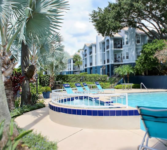 A pool surrounded by trees and chairs.