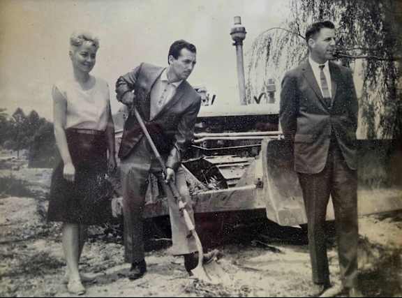 A man with a shovel standing in front of a bulldozer with two other people. 
