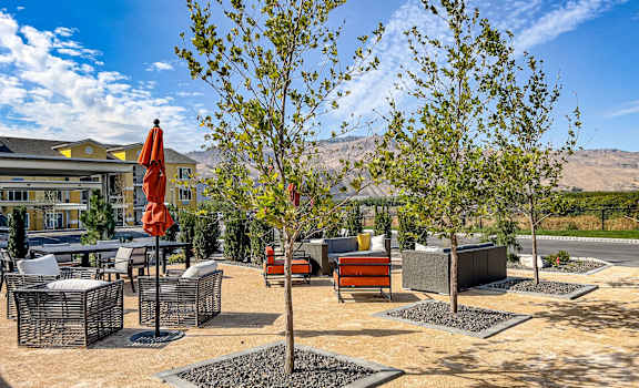 A courtyard with plush chairs, tables, umbrellas, and trees, with the apartment buildings and mountains in the background at LIVEasy Apartments. 