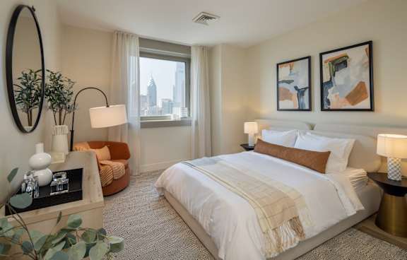 A bedroom with a large bed, a round mirror, and a view of the city.