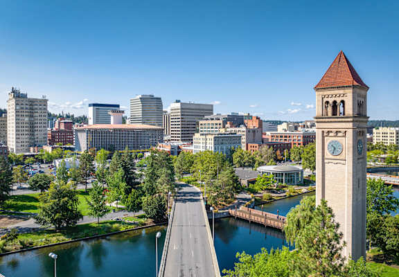 A cityscape with a clock tower in the foreground and a bridge crossing a river.