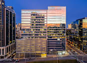 Thumbnail 1 of 24 - A modern glass building with a parking garage in front of it.