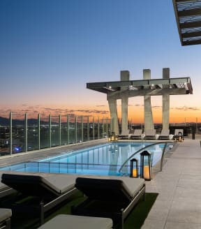 a swimming pool on the top of a skyscraper overlooking a city at dusk
