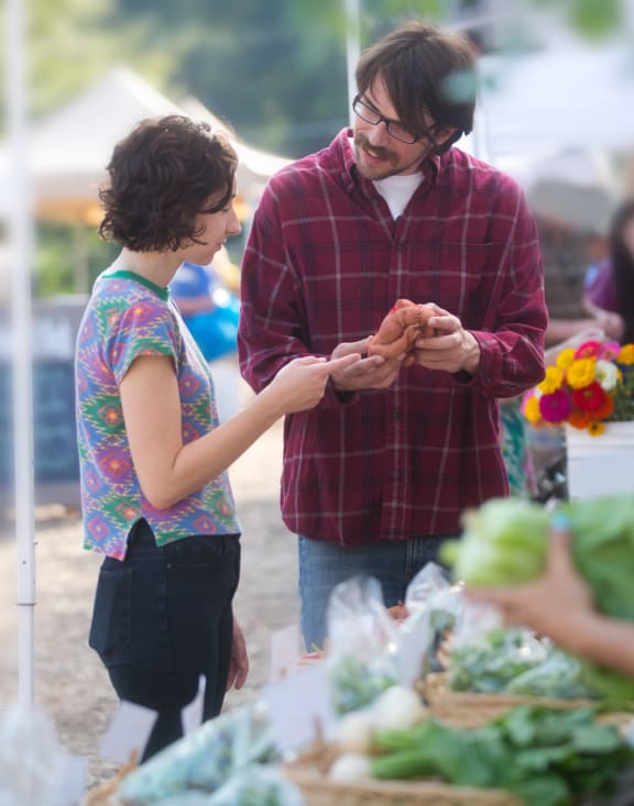 a man and a woman standing in front of a table of vegetables at a farmers market