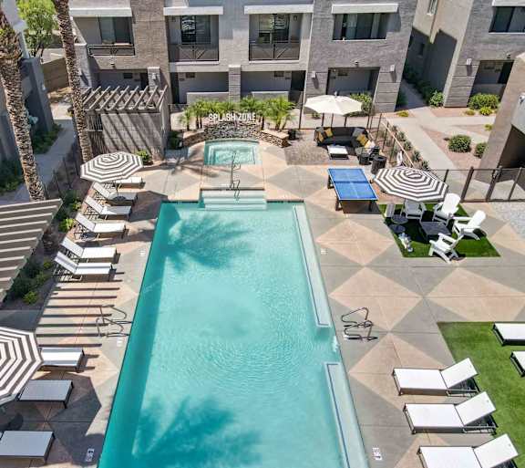 A swimming pool surrounded by lounge chairs and umbrellas in a residential area.