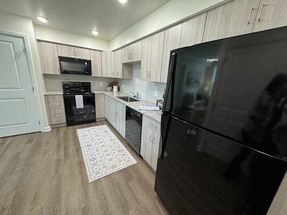 A modern kitchen with a black fridge and wooden cabinets.