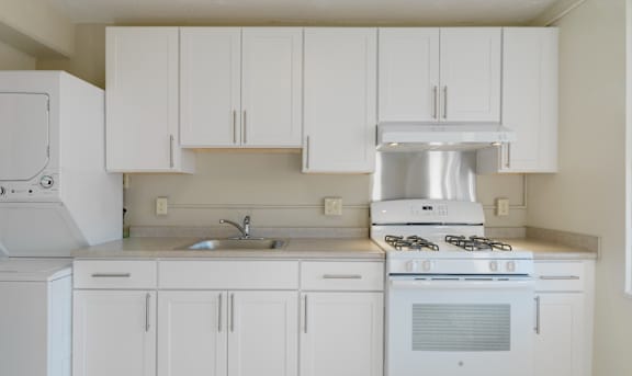 A white kitchen with a stove, sink, and cabinets at Camden Apartments, Boston, 02118