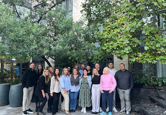 A group of people are standing in front of a building with trees.