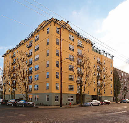 A yellow building with a green base and a parking lot in front.