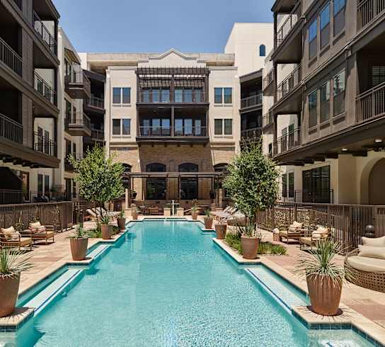A large pool in the middle of a courtyard surrounded by potted plants and lounge chairs.
