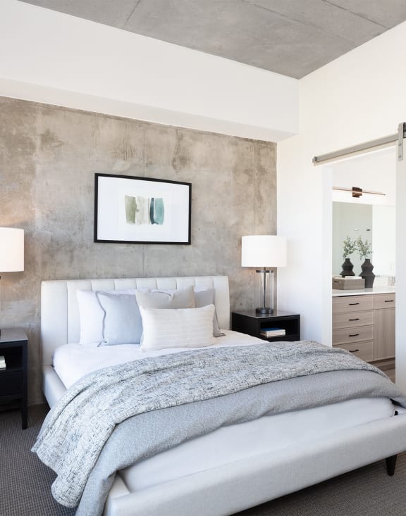 a bedroom with a white bed and a concrete wall