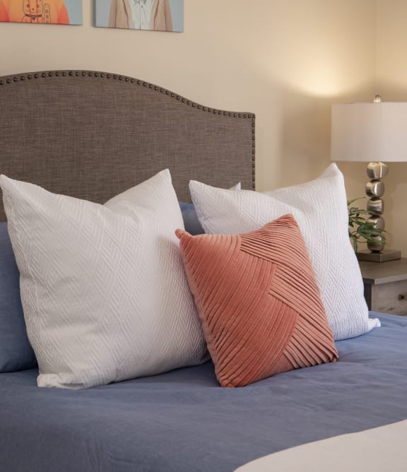 a bed with blue sheets and pillows and a brown headboard at Stoneridge Apartments in Gainesville, 32608