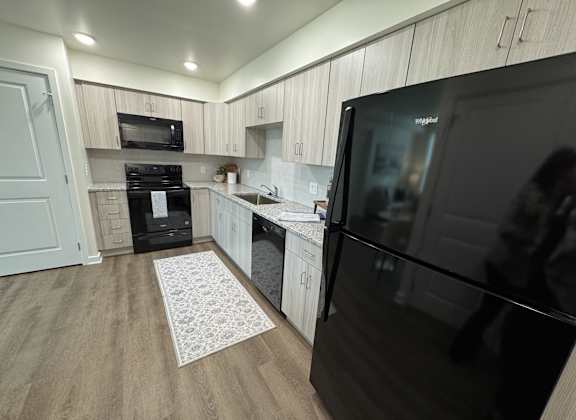 A modern kitchen with a black fridge and wooden cabinets.