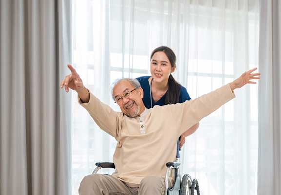 A woman is pushing an elderly man in a wheelchair.