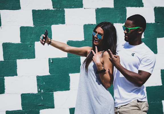 A man and a woman taking a selfie in front of a green and white wall.