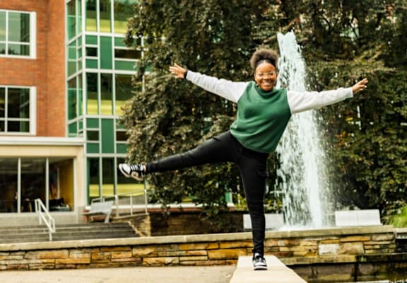 A woman balances on a board in front of a waterfall.