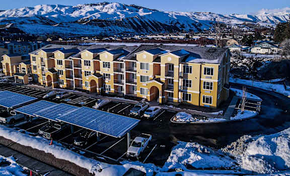 An arial view of the buildings and parking lot of LIV Easy Street Apartments with mountains in the background. 
