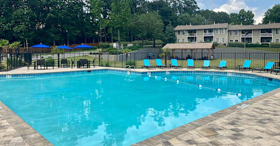 A large swimming pool surrounded by trees and a building in the background.