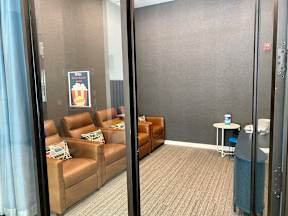 A community media room with 4 movie-theater style chairs and pillows in front of a large TV and TV console.