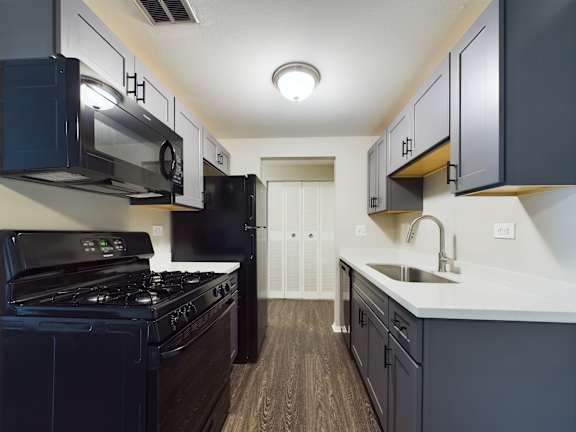 A modern kitchen with dark wood floors and black appliances.