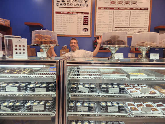 a man standing behind the counter of a display case of donuts