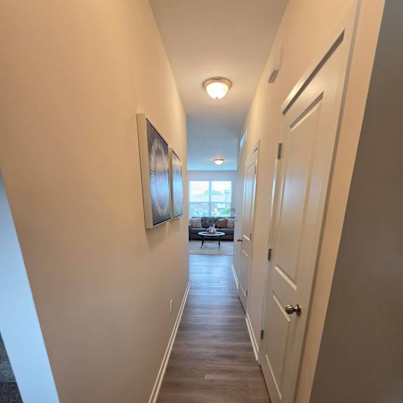 A long, empty hallway with a light on the wall and a window in the distance.