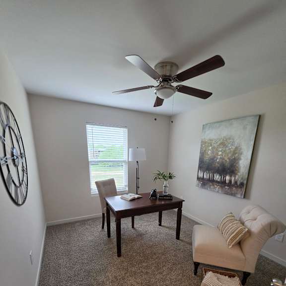 A living room with a fan, a couch, and a painting on the wall.