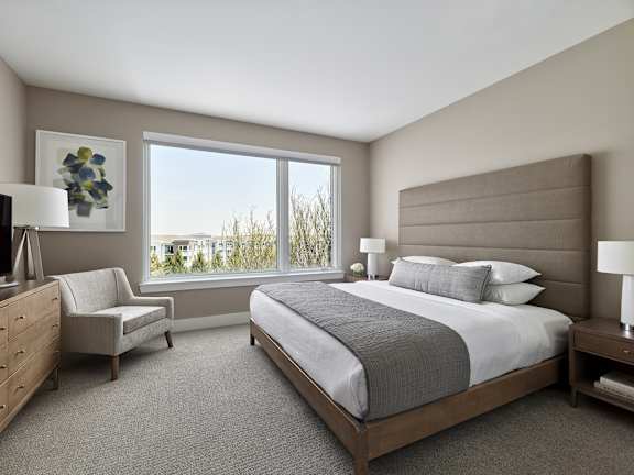 A bedroom with a large bed, a chair, and a desk with a lamp.