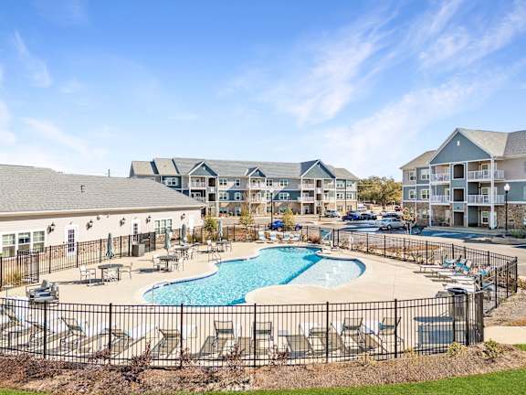 A large outdoor pool surrounded by a black fence and lounge chairs.