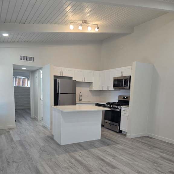 A modern kitchen with a white countertop and a grey stone wall.