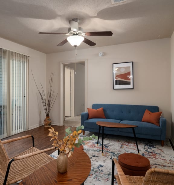 a living room with a blue couch and a ceiling fan at The Fountains Apartments, Pensacola, FL