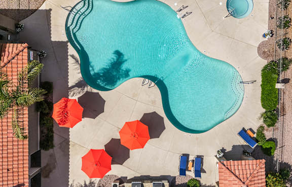 An aerial view of a pool with a blue water feature and orange umbrellas.