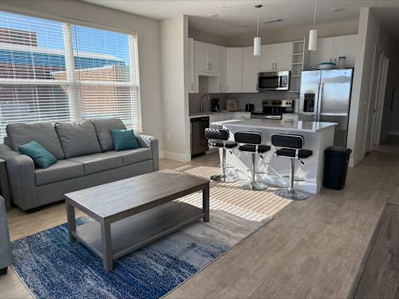 A modern kitchen with a bar stool and a grey couch.