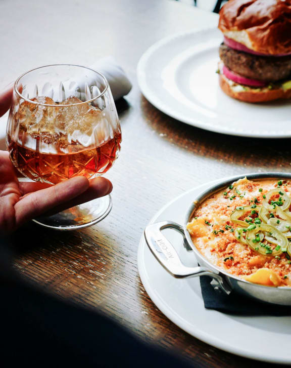 a person holding a glass of beer in front of a plate of food at East 4th Street, Cleveland, 44115