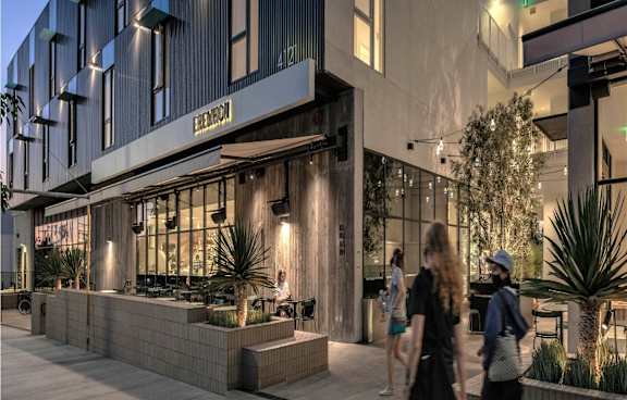 A modern building with a bar on the ground floor and people walking by.