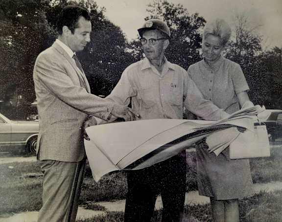 Three people standing outside reviewing blueprints. 