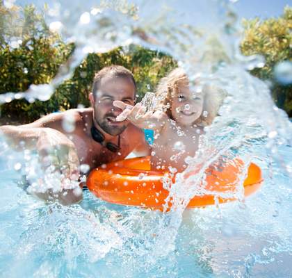 Father Playing with Child in Swimming Pool and Splashing Water