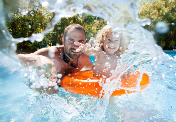 Father Playing with Child in Swimming Pool and Splashing Water