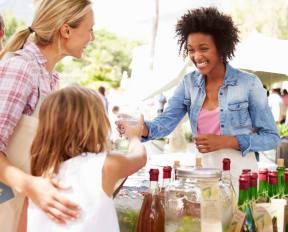 Woman at Outdoor Farmer's Market Selling Soft Drink to Mother and Daughter 