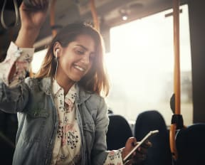 Woman Standing In Bus Looking At Phone and Smiling