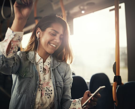 Woman Standing In Bus Looking At Phone and Smiling
