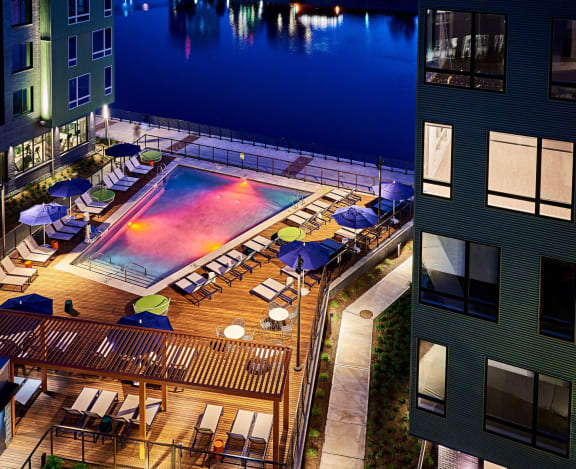 a hotel pool with umbrellas and chairs on a rooftop at night at Dey & Bergen, Harrison, 07029