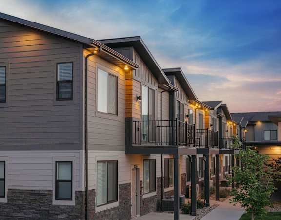A row of modern townhouses with balconies and lights on.