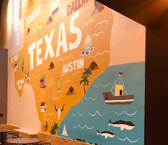 A wall mural depicting various landmarks of Texas, including a lighthouse, a windmill, and a crane.