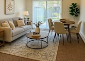 Thumbnail 8 of 8 - A living room with a grey couch, a coffee table, a dining table with chairs, a floor lamp, and a potted plant.