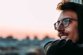A man with glasses and a hoodie stands with his arms crossed.